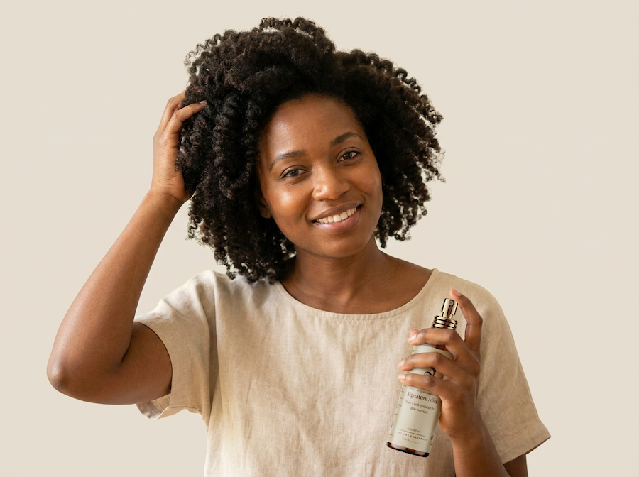Woman holding a Sires Crown Signature Mist hair product spray bottle against a plain background